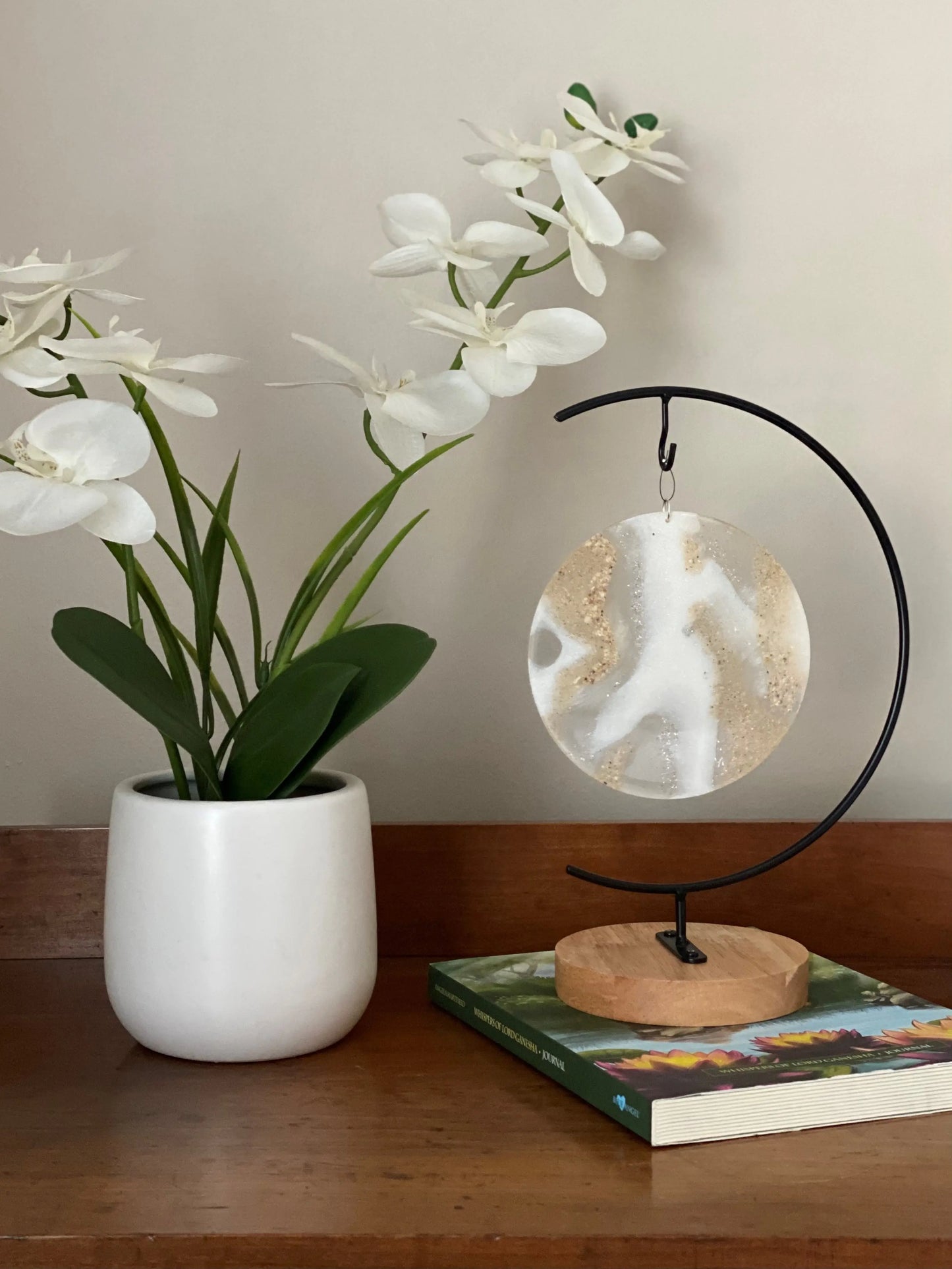 White orchid in a pot on a wooden surface with a decorative memorial ash stand and book.