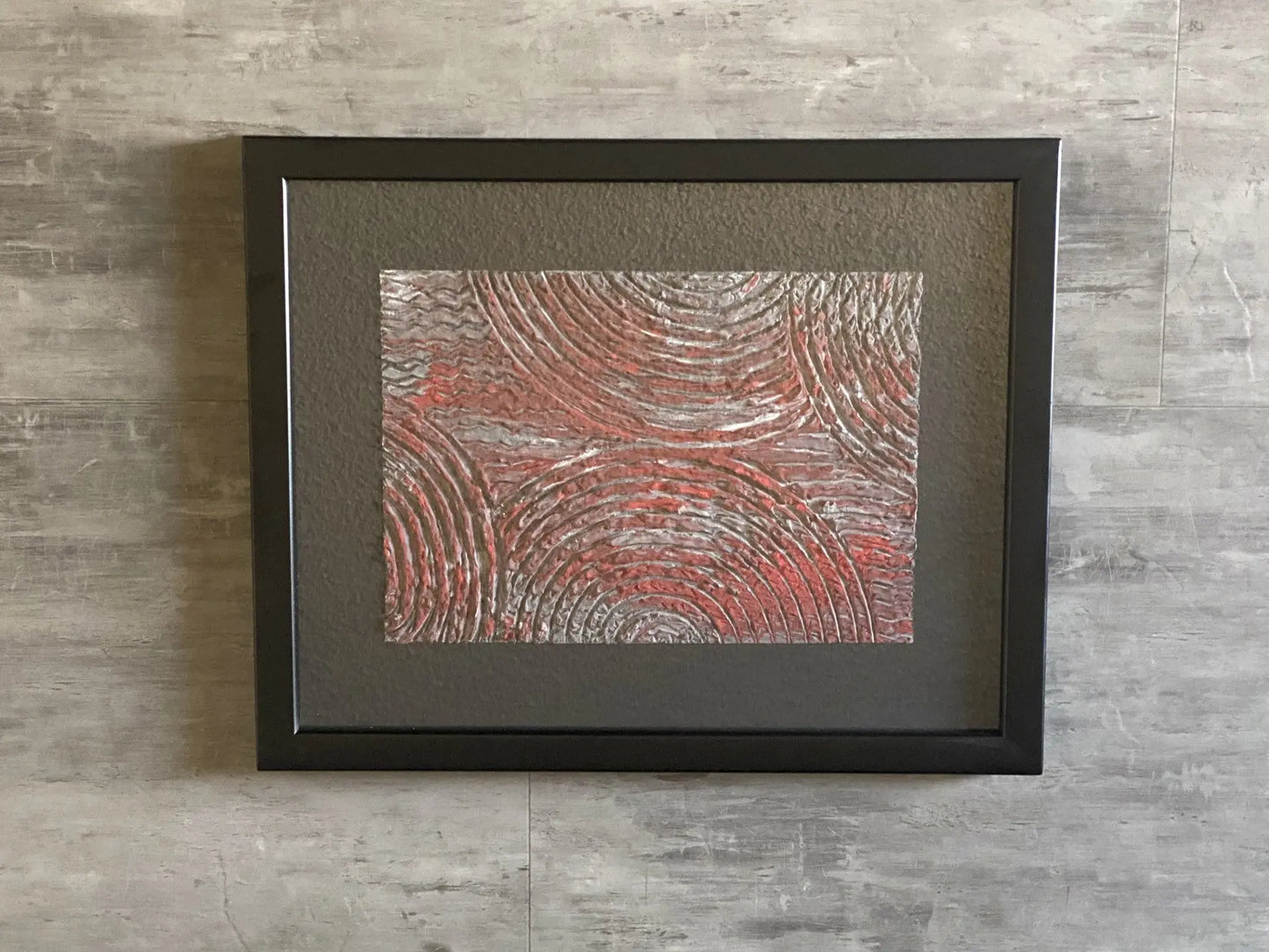Framed textured acrylic resin artwork featuring raised concentric circular patterns in red and grey tones.
