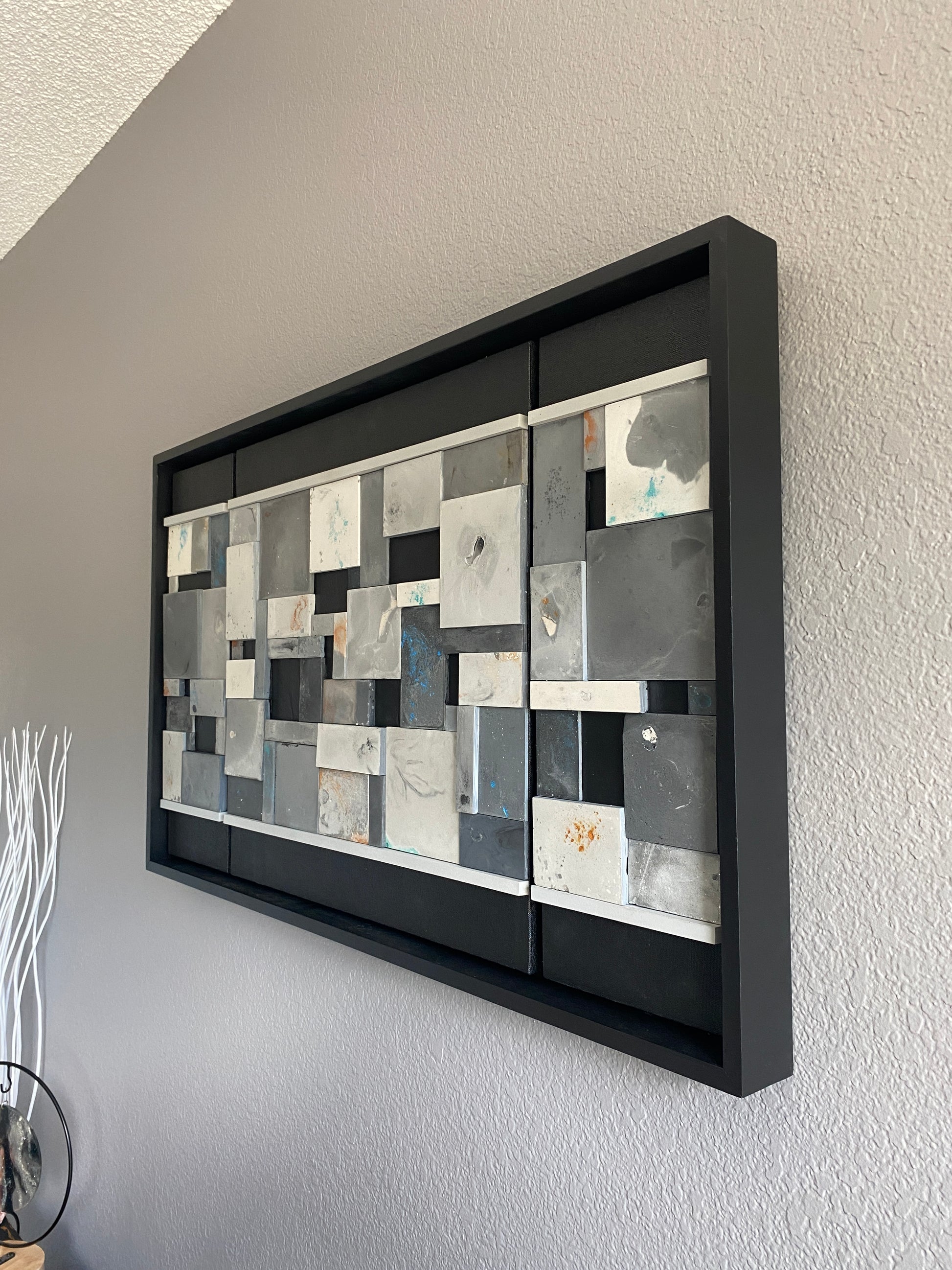 Decorative wallart with geometric pattern in a black frame on a plain wall.