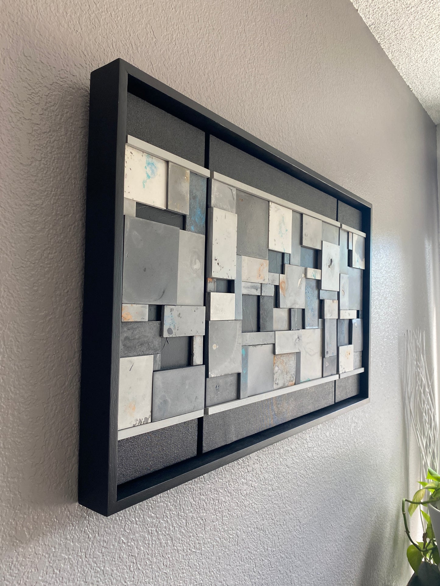Decorative wall art with square tiles in a black frame on a gray surface.