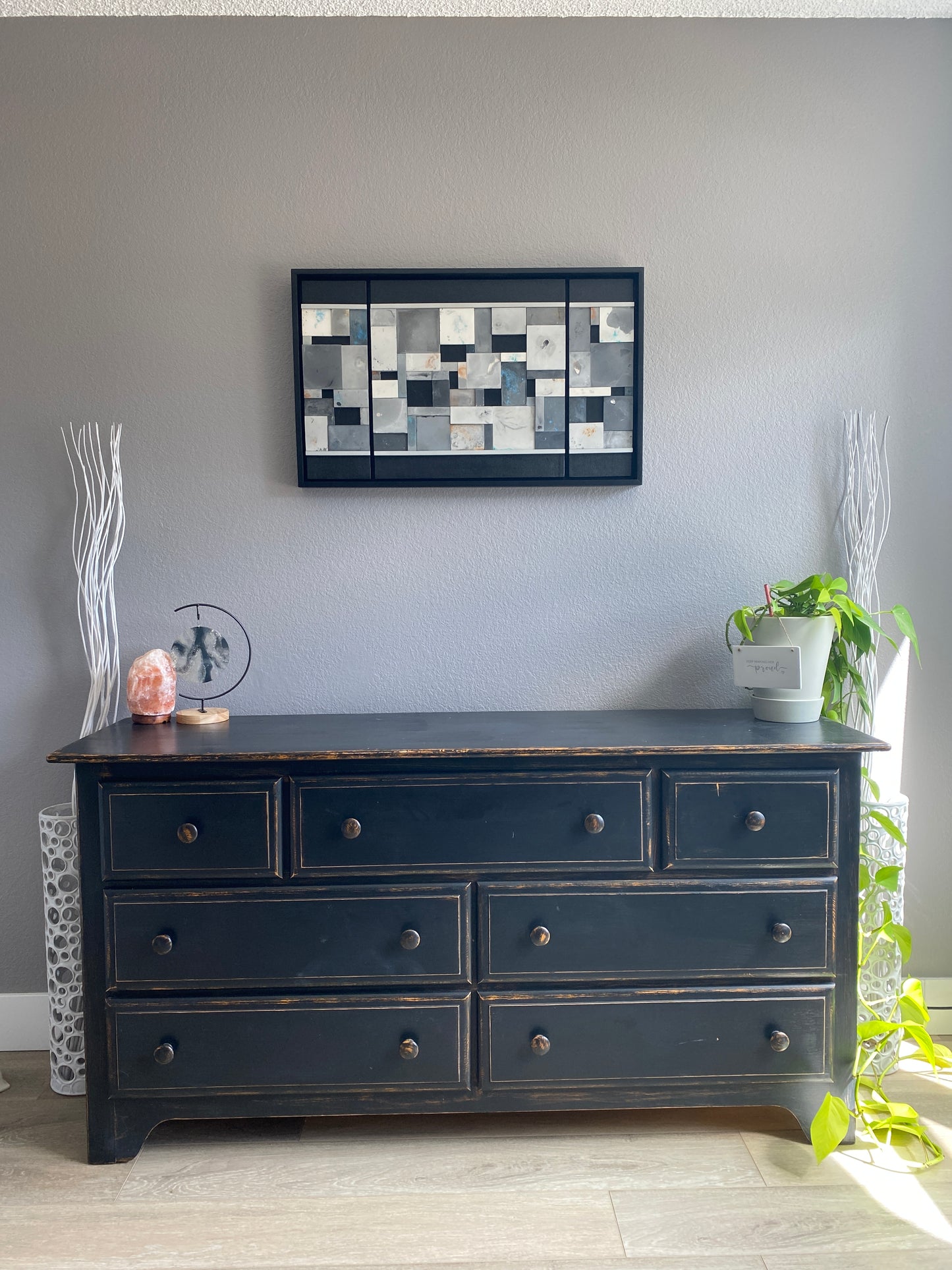 Dark dresser with multiple drawers against a gray wall, with a decorative wallart piect.