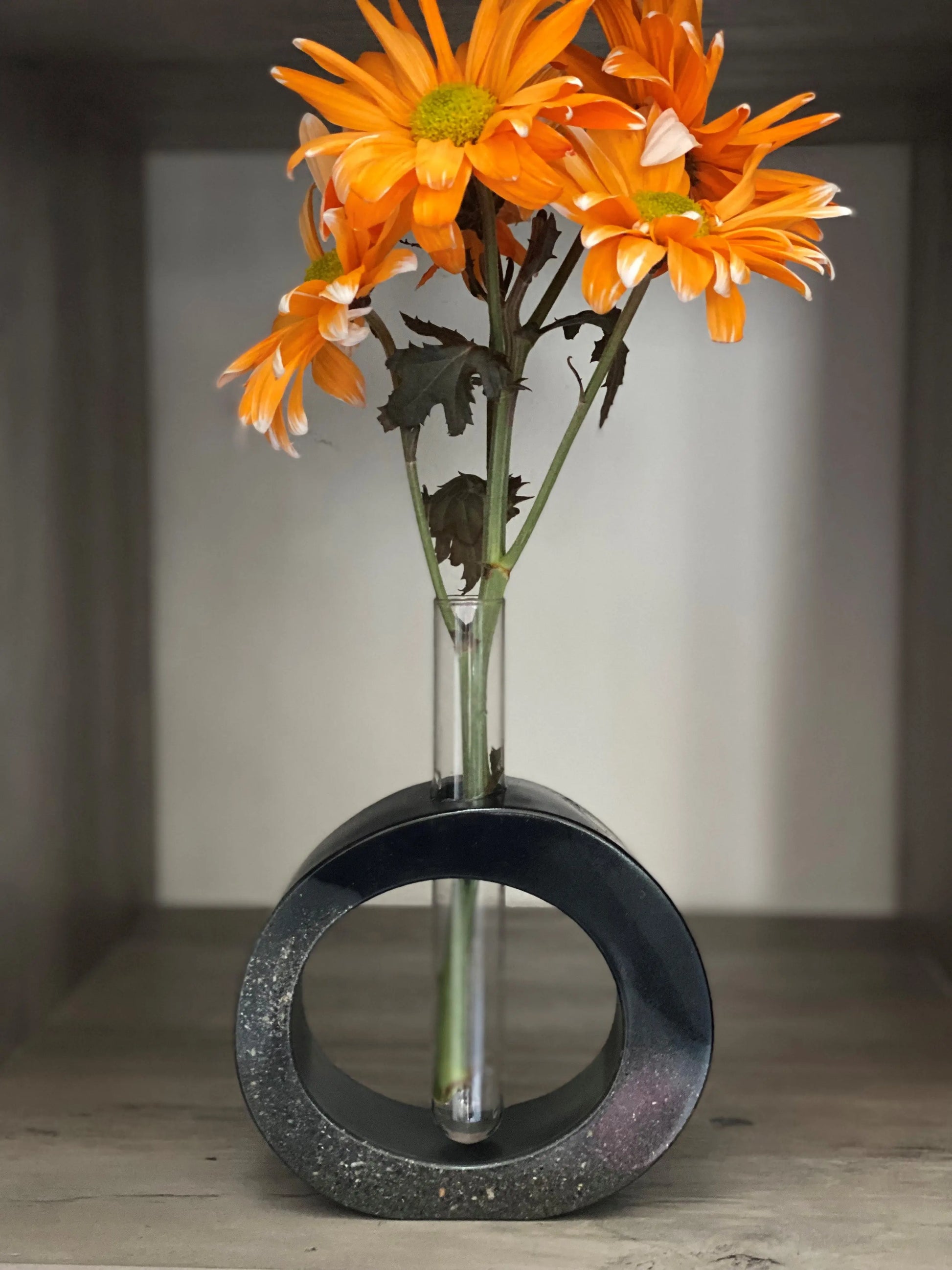 Decorative vase with a circular design holding orange flowers on a neutral background