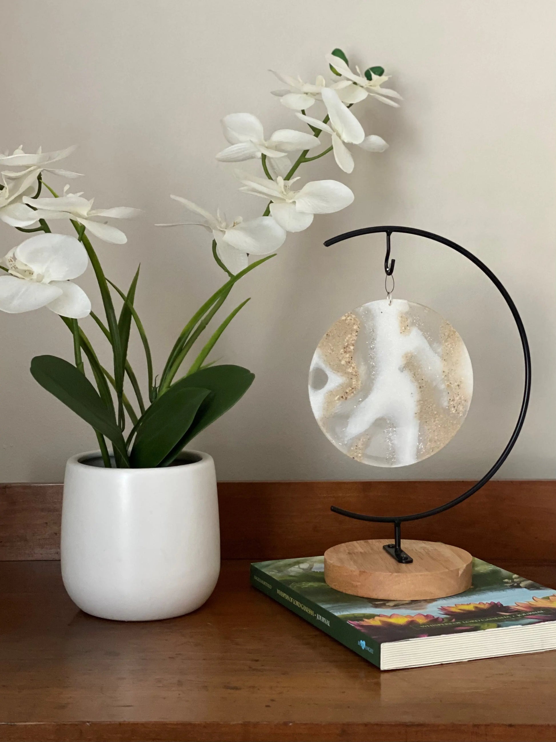 White orchid in a pot on a wooden surface with a decorative memorial ash stand and book.