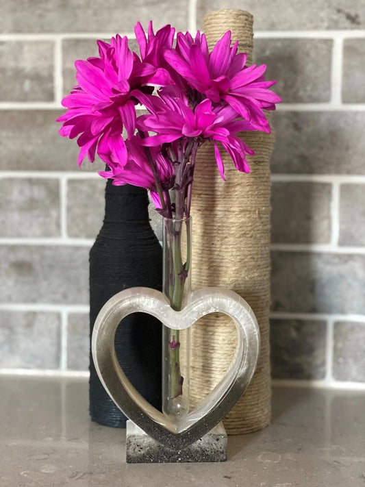 Heart-shaped vase with pink flowers against a tiled wall background