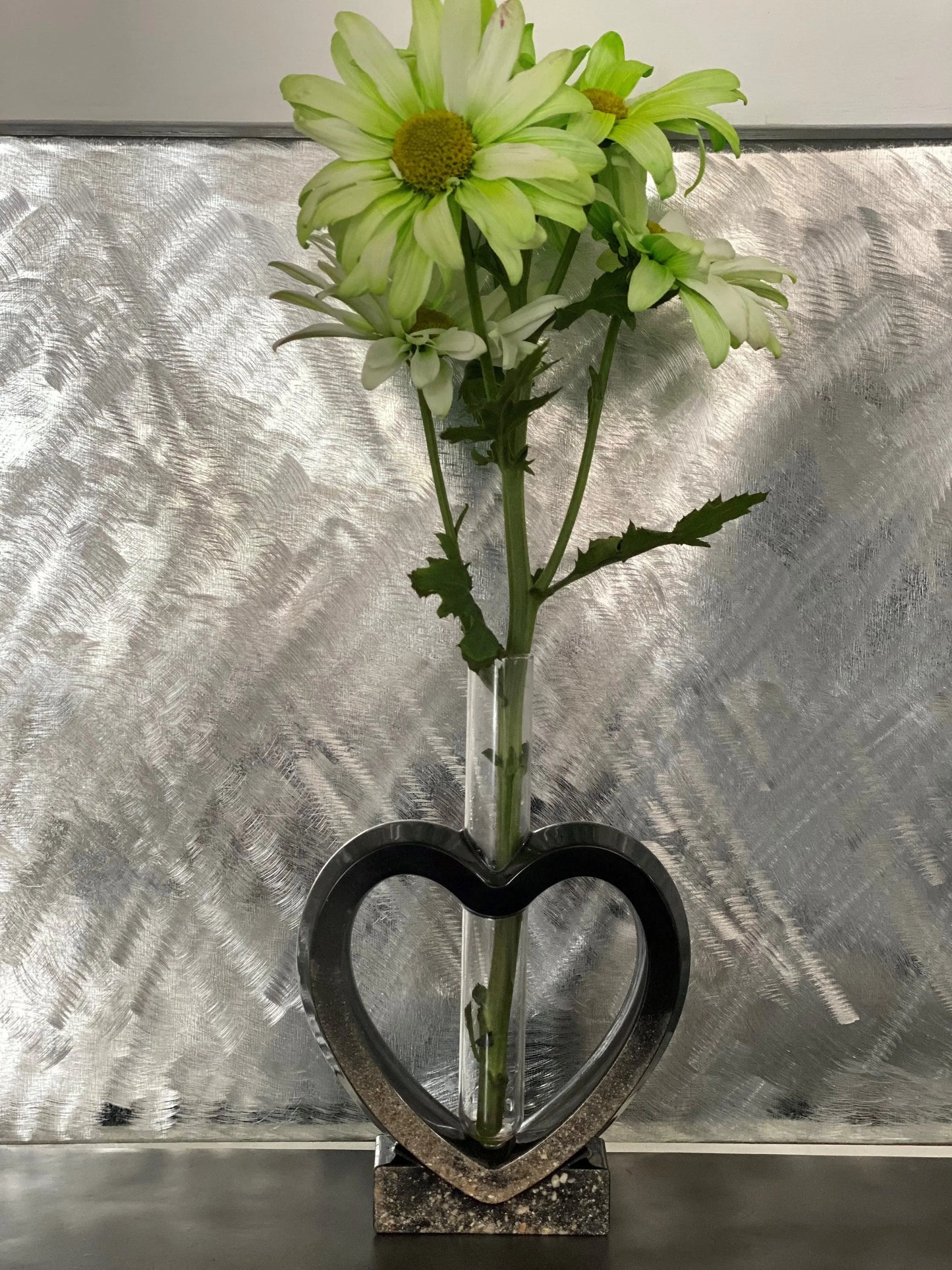Heart-shaped vase with green flowers against a textured silver background