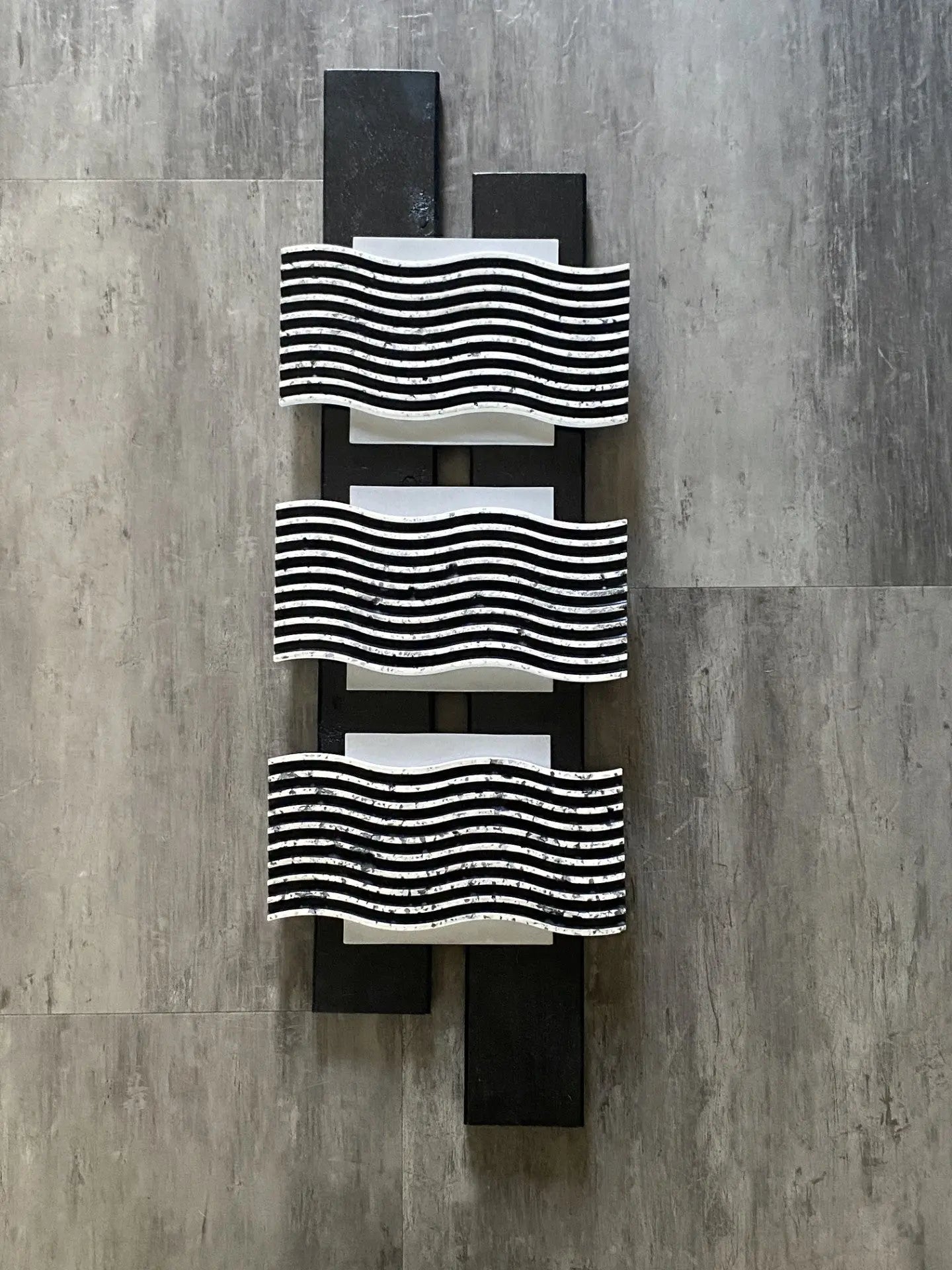 Black and white mixed‑media artwork featuring three resin wave forms layered over a geometric wood frame.