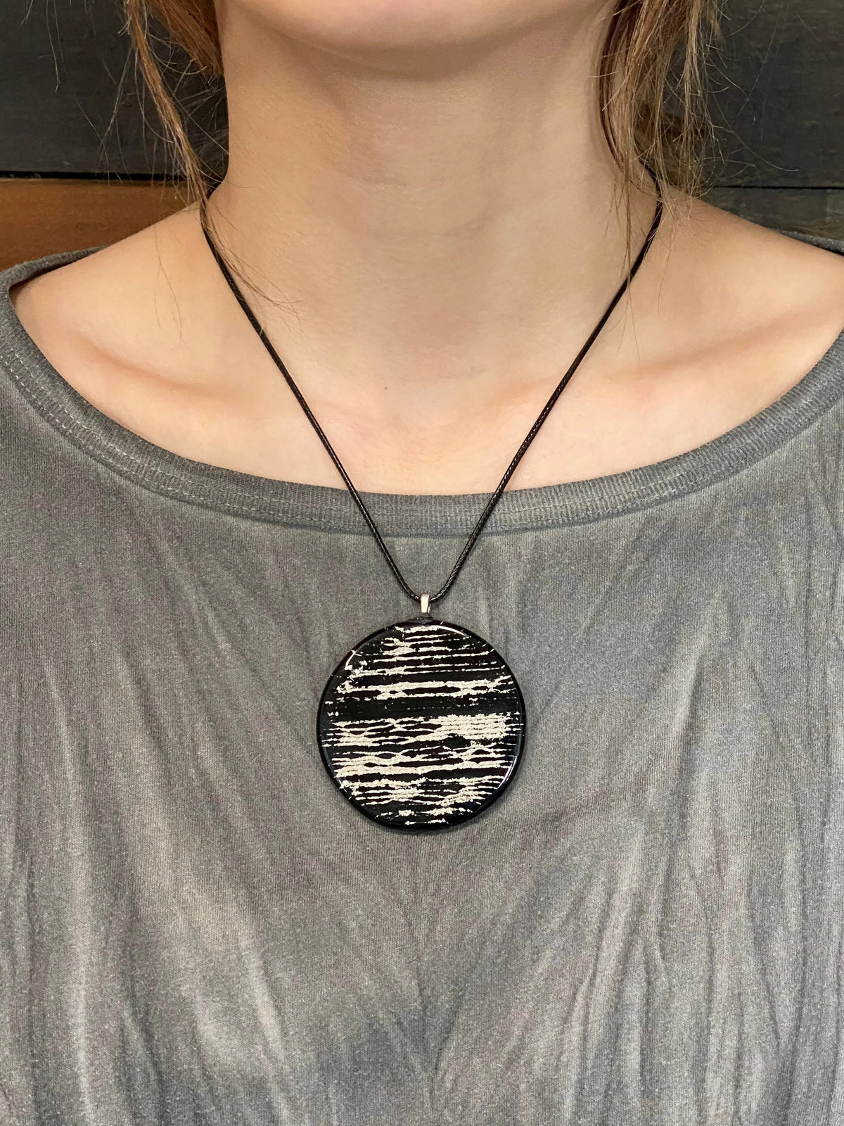 Person wearing a gray shirt with a black ash-infused patterned pendant necklace.