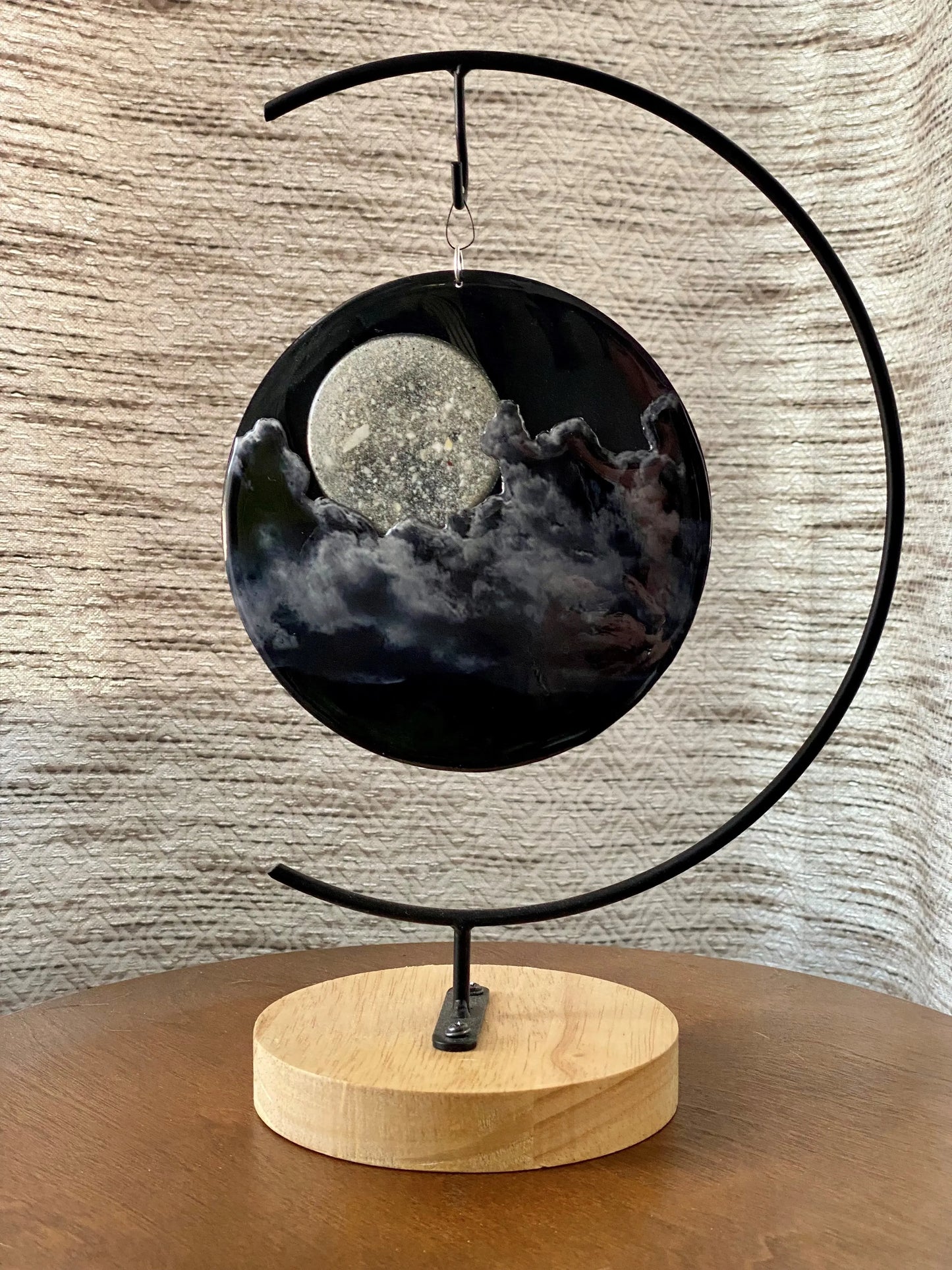 Decorative moon and clouds with a black metal arch and a wooden base on a textured wall background