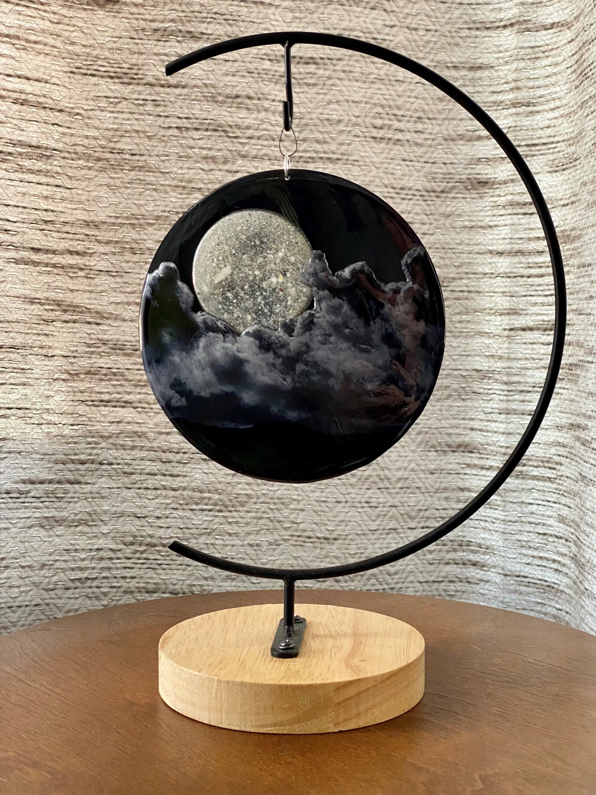 Decorative moon and clouds with a black metal arch and a wooden base on a textured wall background