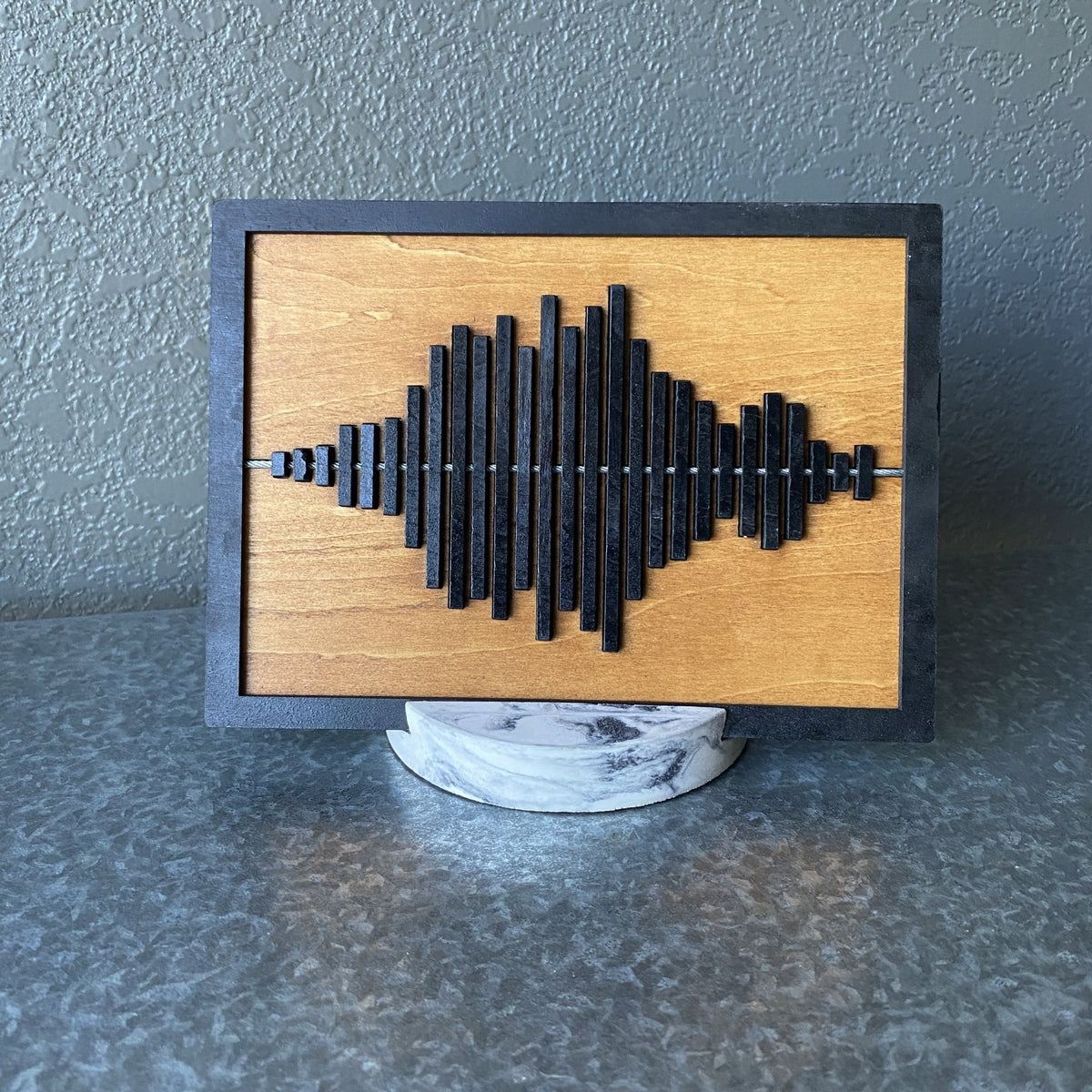Stained wooden display piece with black sound wave and round marbled stand.