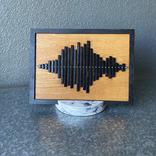 Stained wooden display piece with black sound wave and round marbled stand.