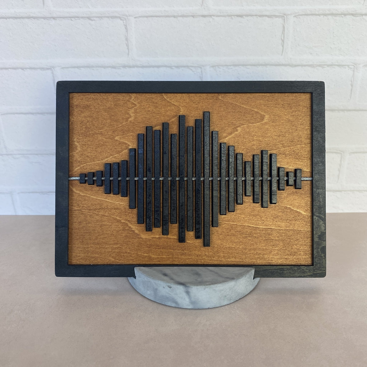 Black framed sound wave with warm tone stained wood and round marbled stand.