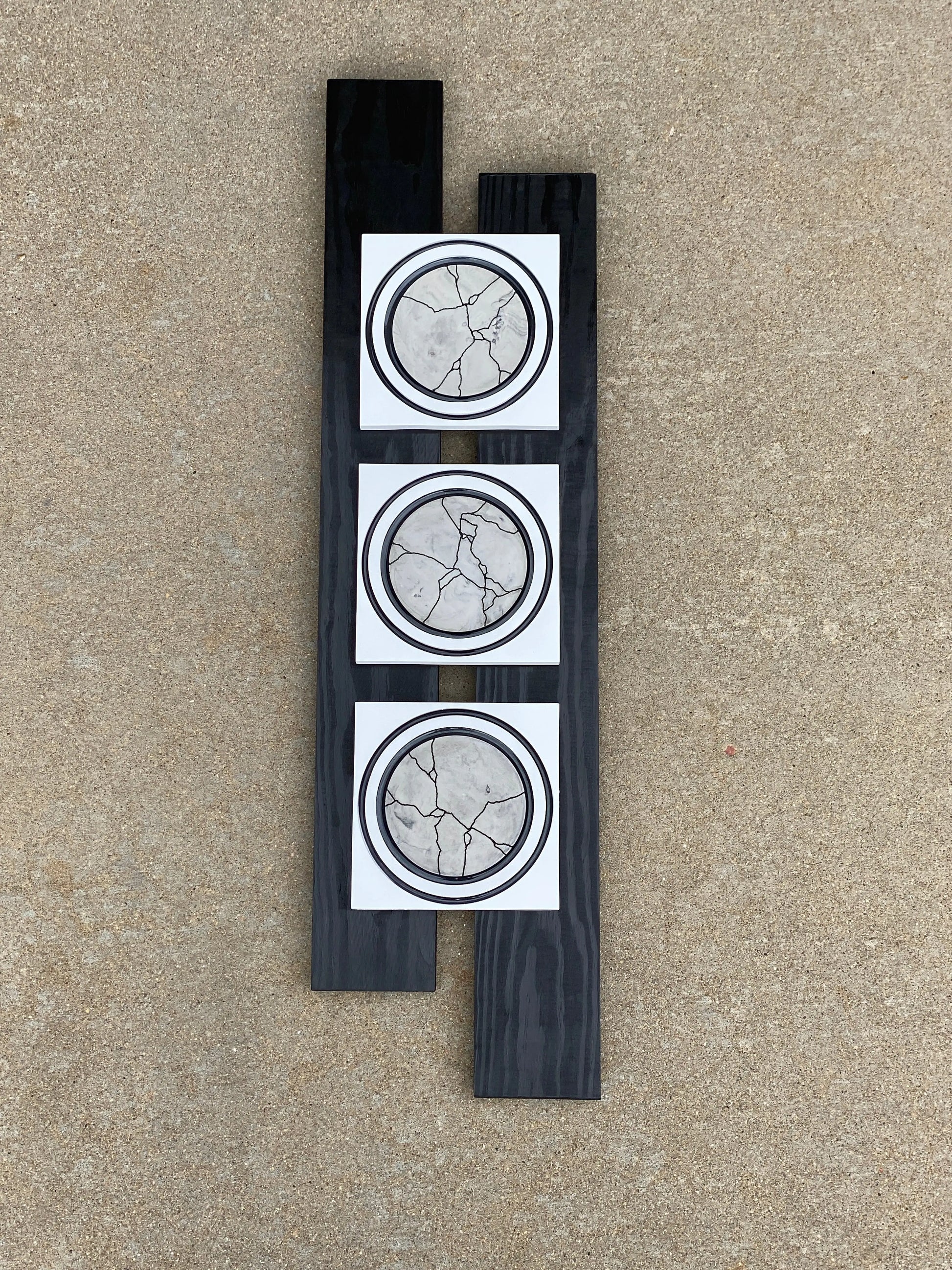 Mixed‑media artwork featuring three circular resin pieces with crack‑like patterns mounted on a staggered black wooden base.