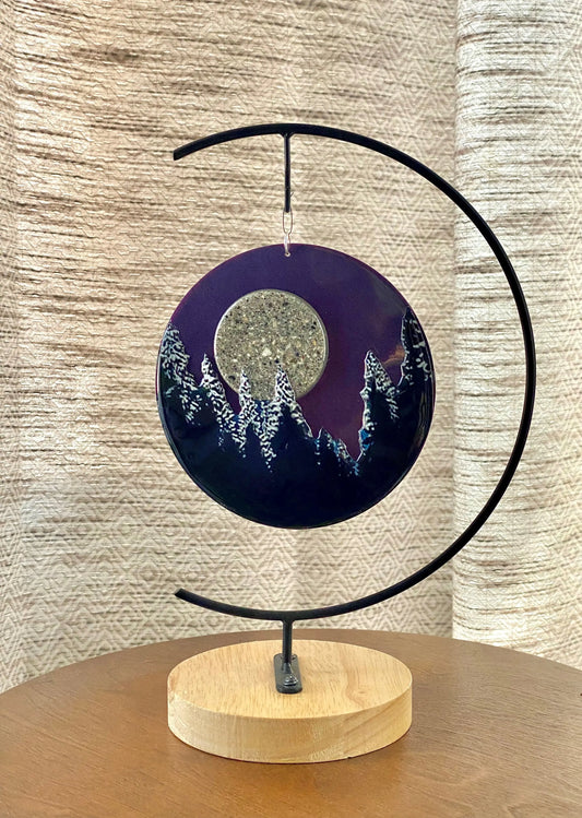 Decorative piece with a circular design featuring a moon and trees on a wooden base, against a textured beige wall.