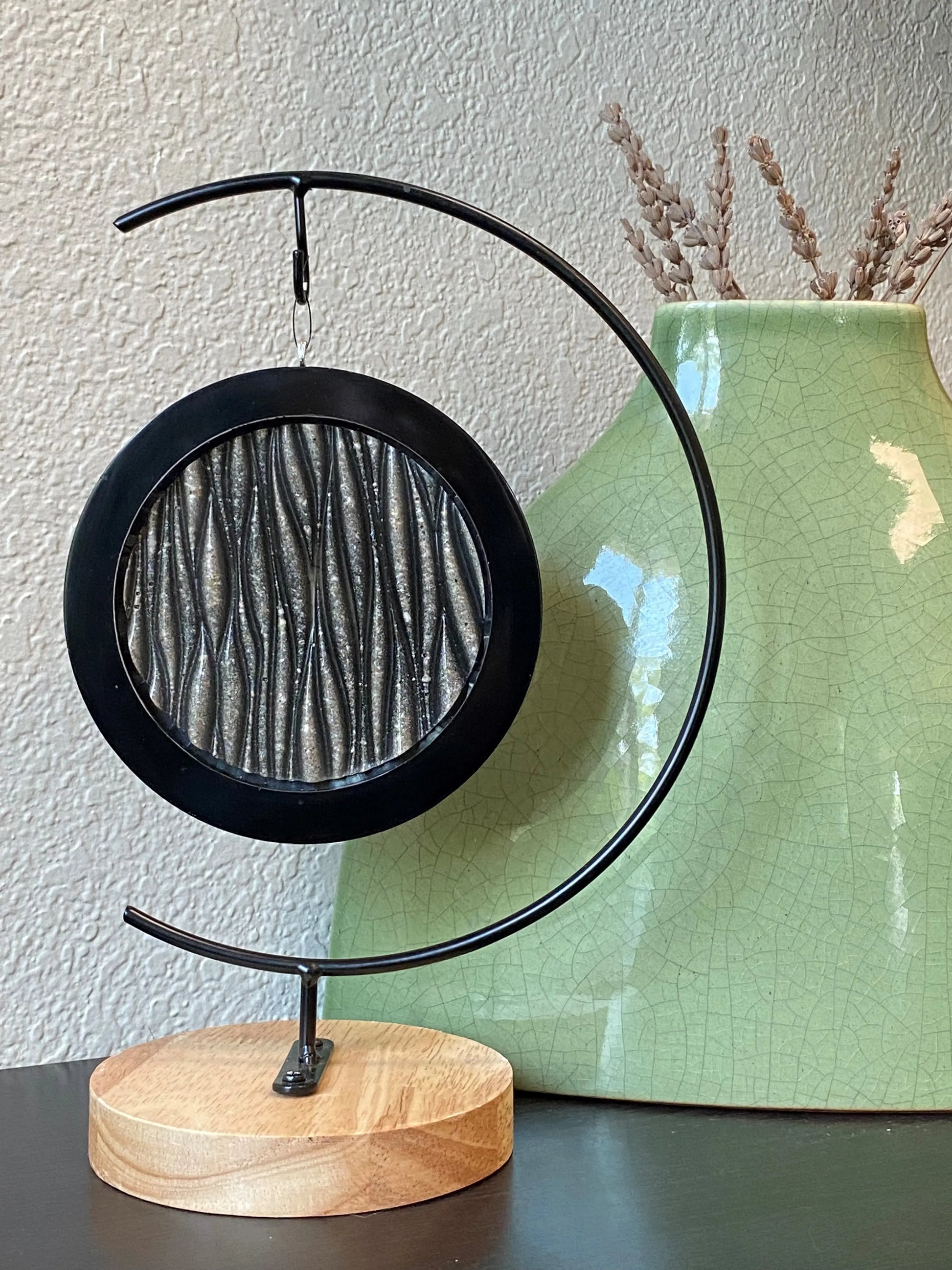 Geode waves on black metal stand with ashes infused next to a green vase.