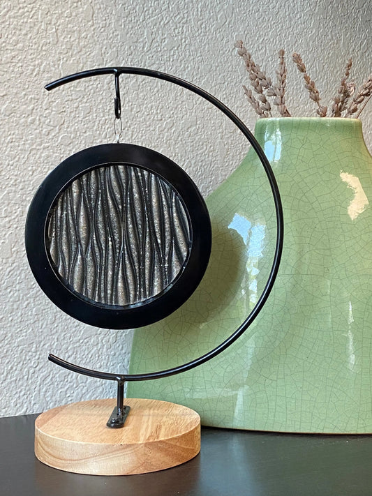 Geode waves on black metal stand with ashes infused next to a green vase.