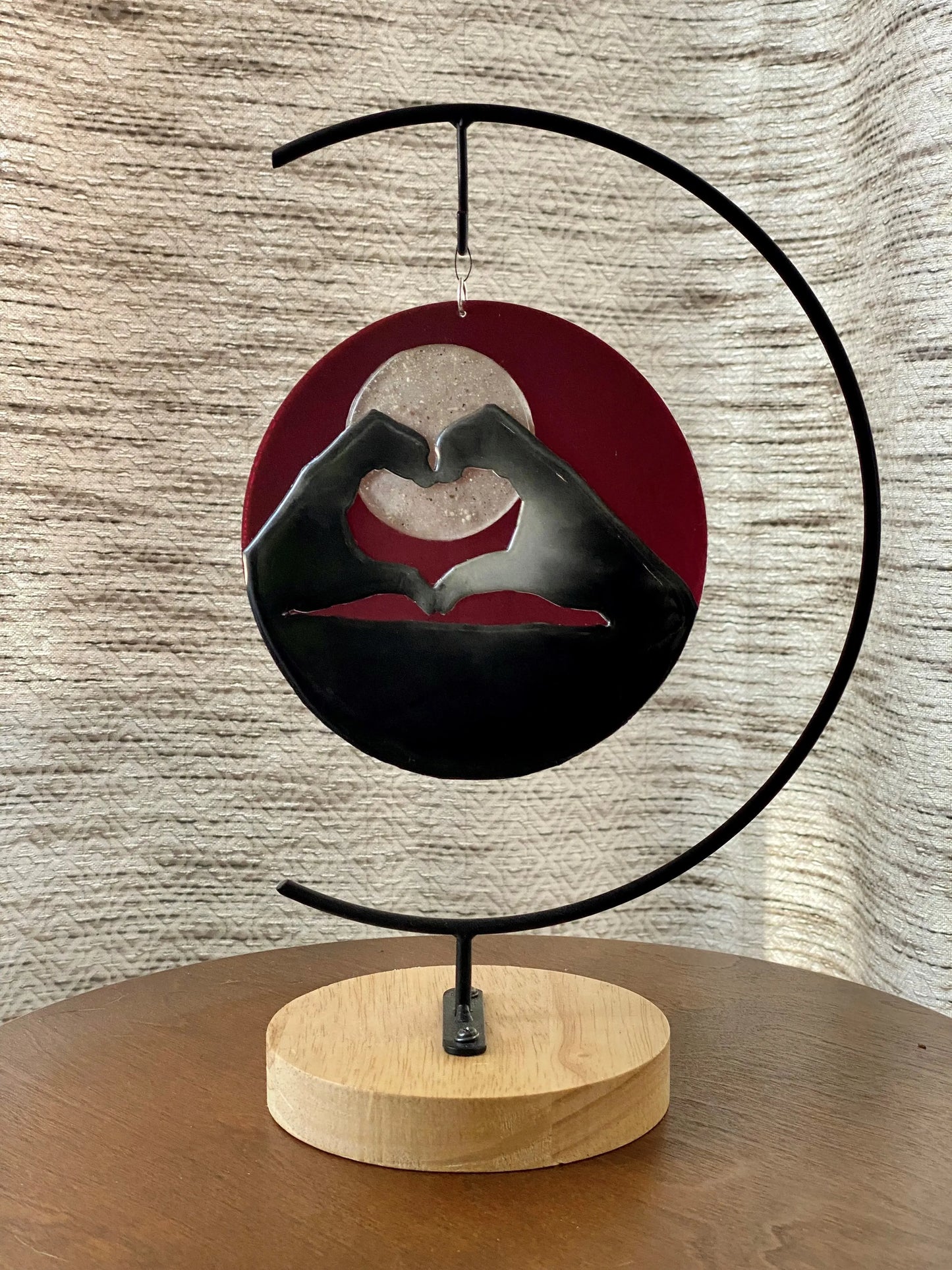 Decorative piece with hands forming a heart shape on a wooden base against a textured wall.