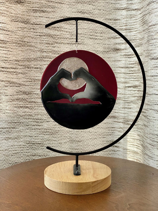 Decorative piece with hands forming a heart shape on a wooden base against a textured wall.