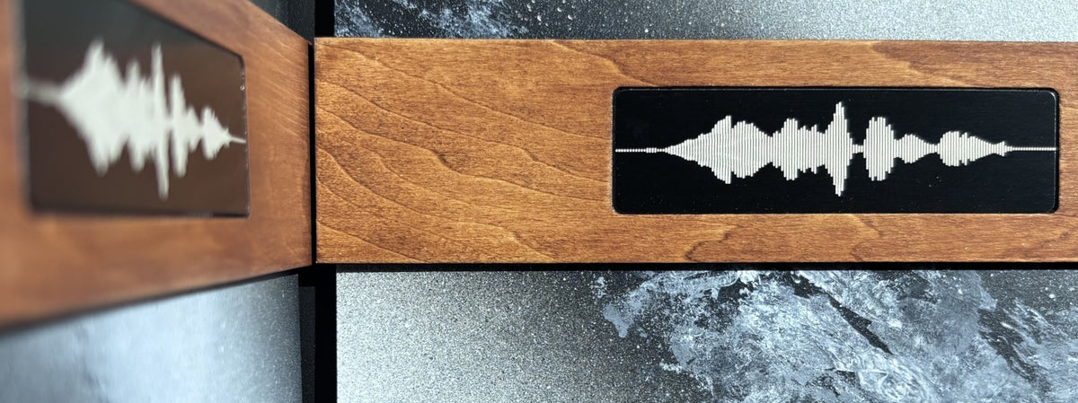 A close-up of a wooden keepsake box or album with a black plaque featuring a white soundwave design, set against a dark textured surface.