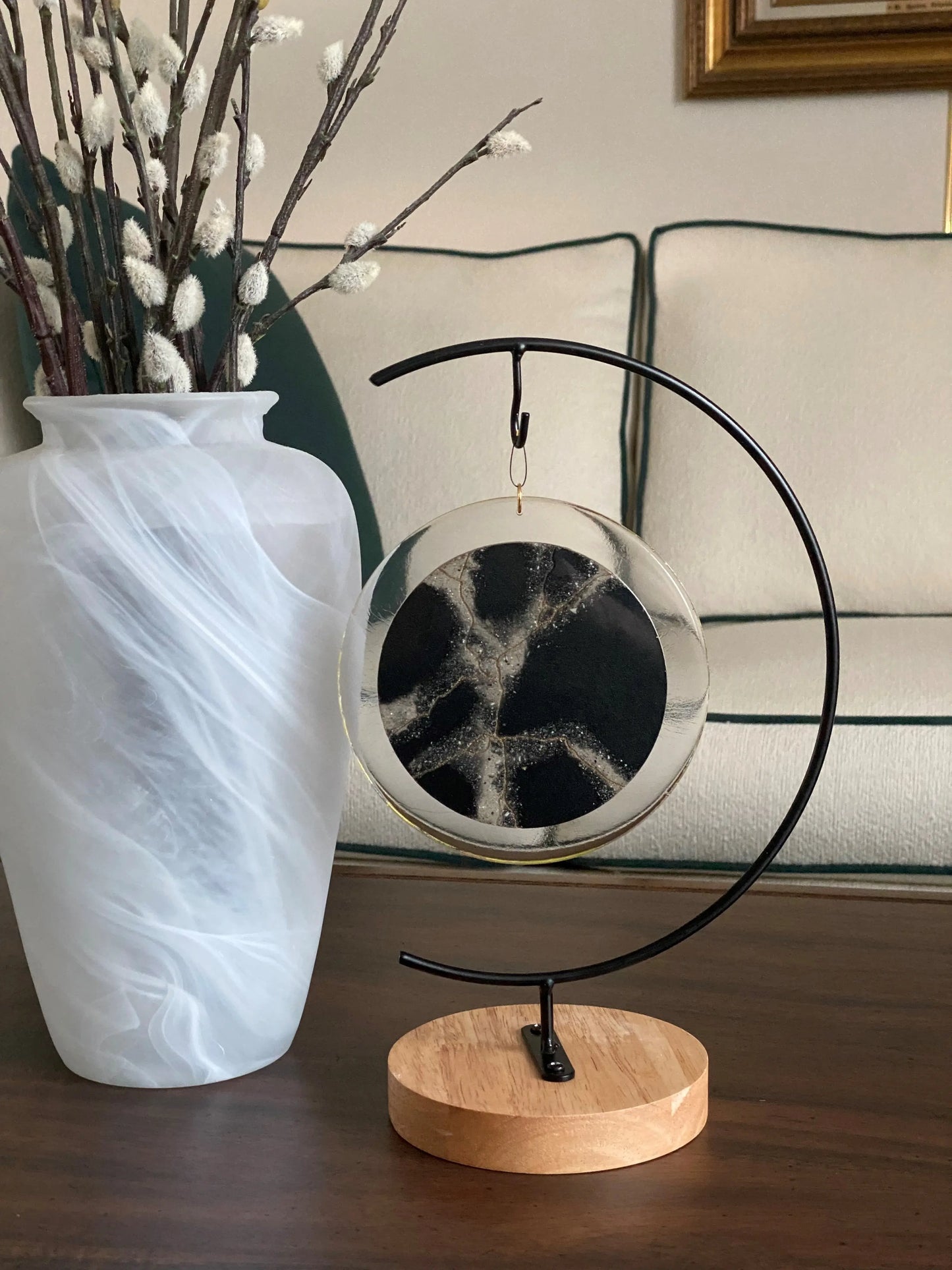 Decorative ash infused black circle with a vase and branches on a wooden surface.