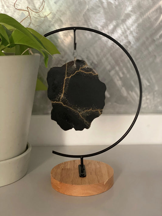 Decorative black ash infused geode on a wooden stand with a plant in the background
