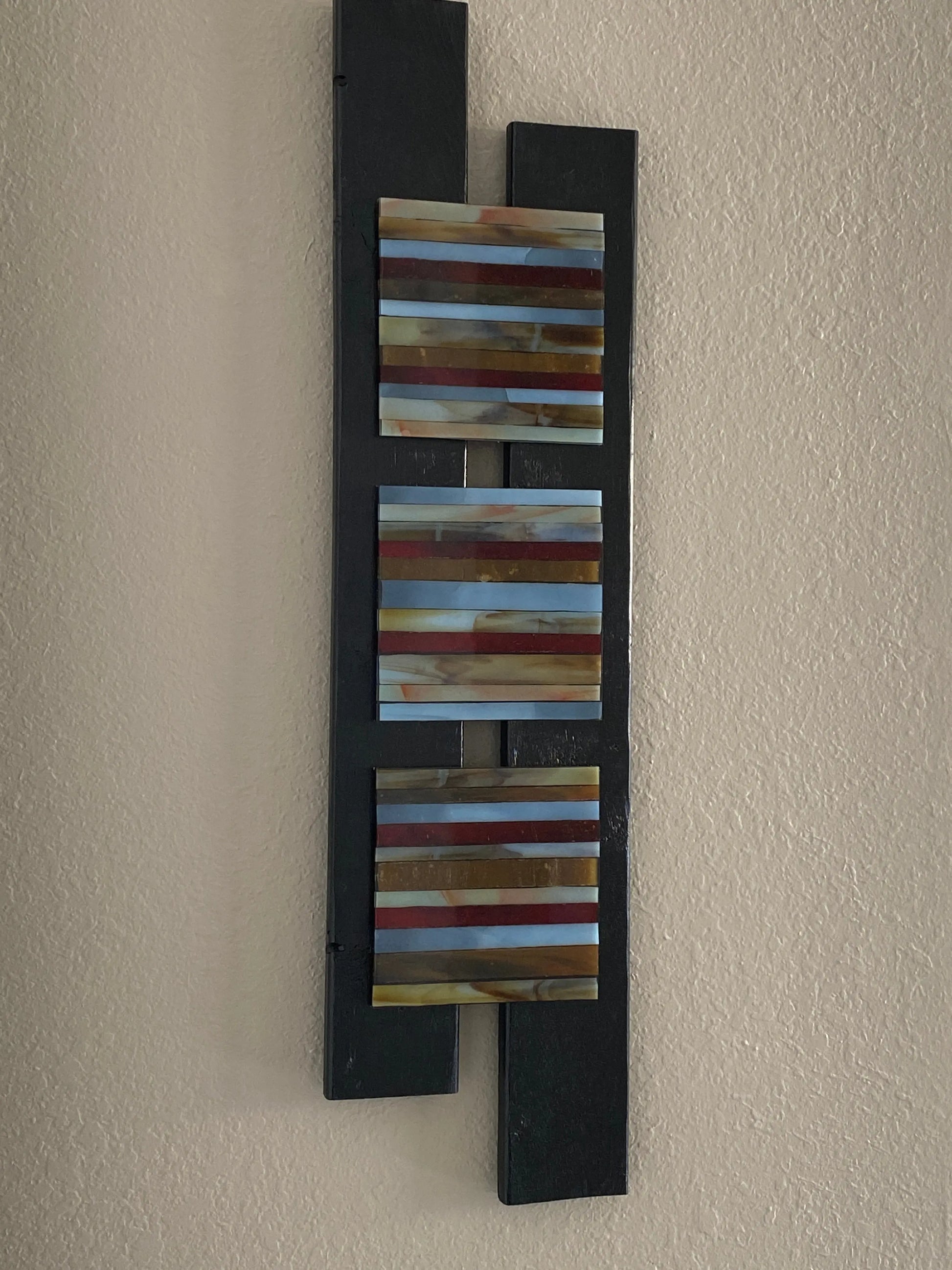 Mixed‑media artwork with three resin panels containing hand‑cut glass strips in vertical color patterns, mounted on a staggered wooden base.