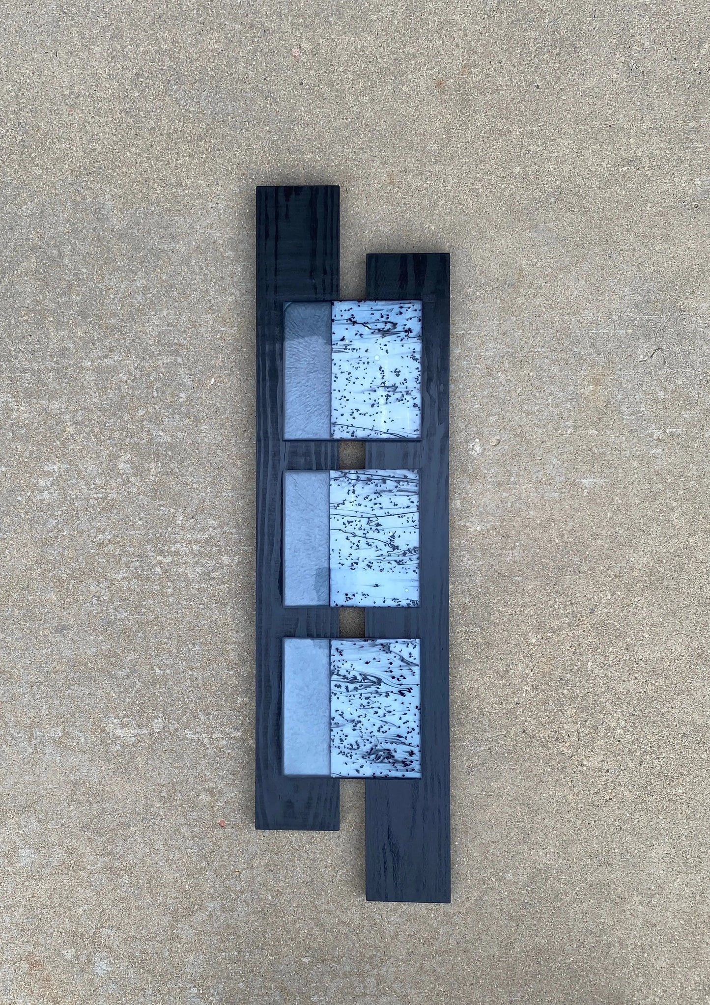 Mixed‑media artwork with three panels featuring confetti black‑and‑white glass infused in resin, paired with solid surfaces and mounted on a geometric wooden frame.