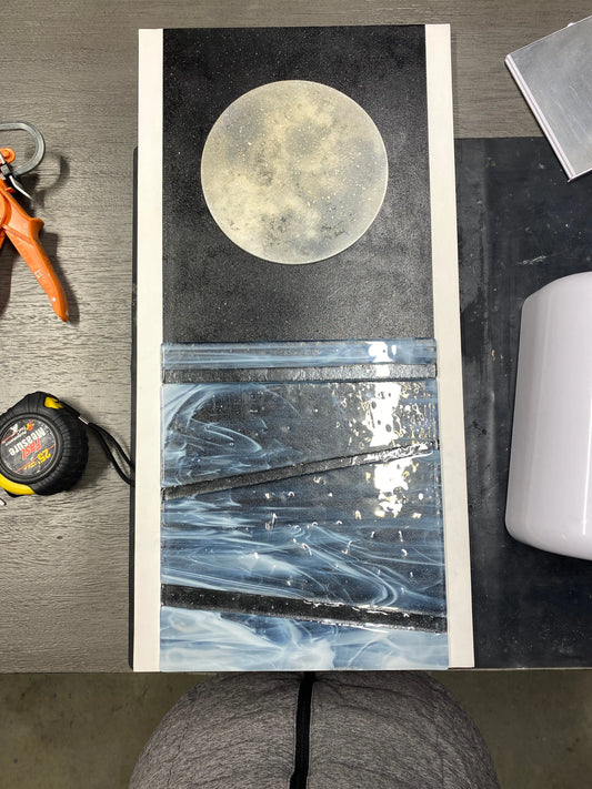 Mixed‑media artwork featuring a resin moon infused with ashes and frosted glass water elements, created as a memorial piece for a family member.