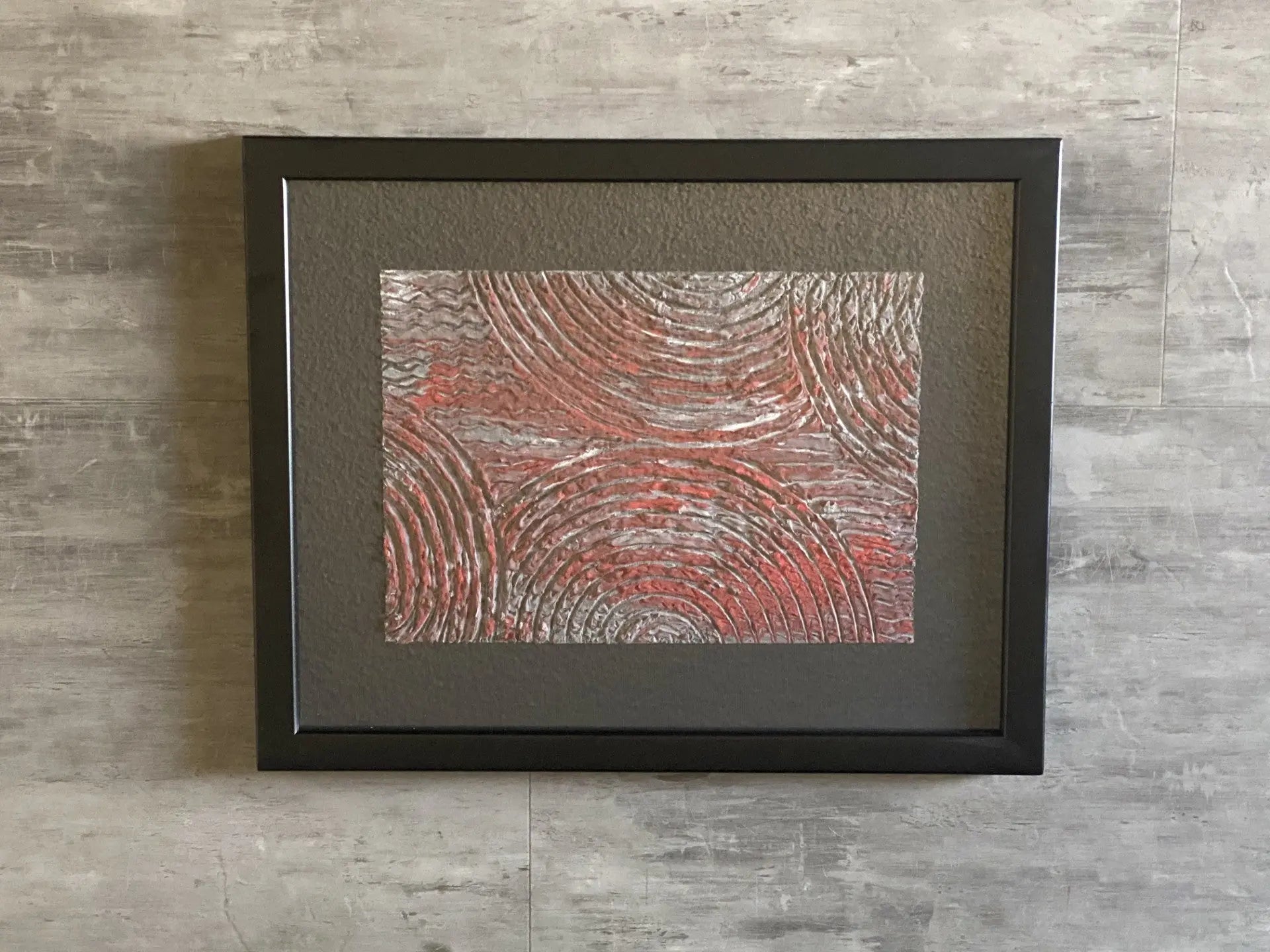 Framed textured acrylic resin artwork featuring raised concentric circular patterns in red and grey tones.