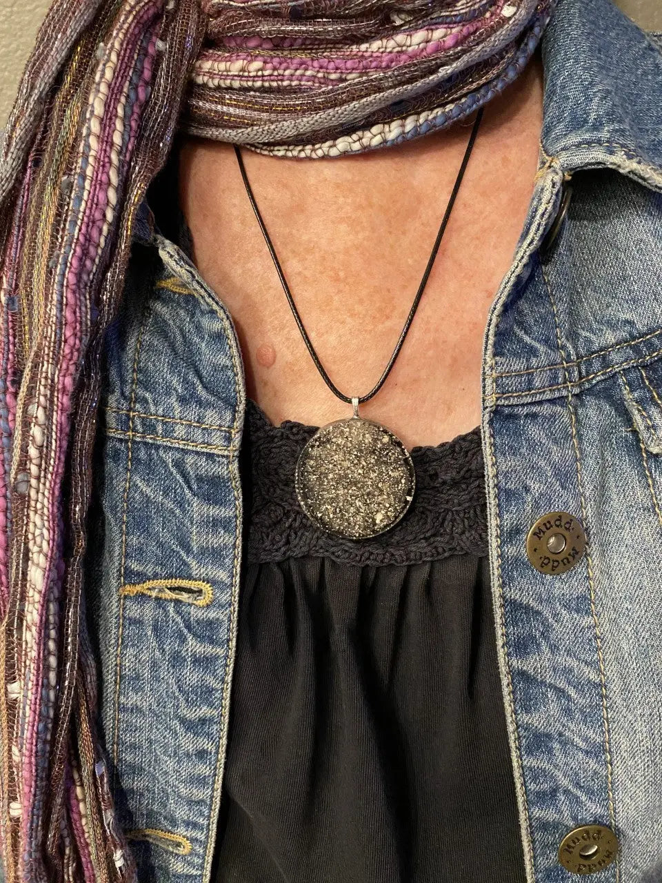 Person wearing a denim jacket, black top, and colorful scarf with a necklace.