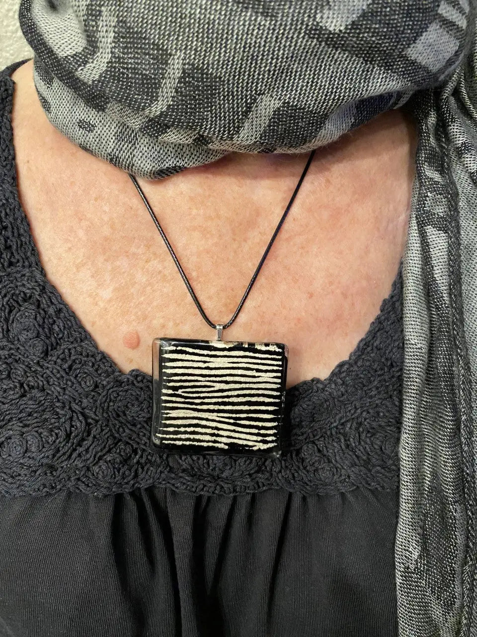 Person wearing a black shirt with lace details and a rectangular pendant necklace.