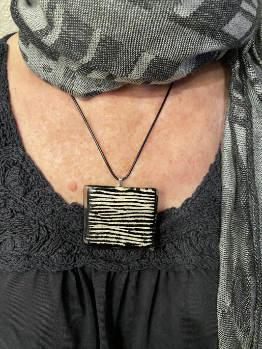 Person wearing a black shirt with lace details and a rectangular pendant necklace.