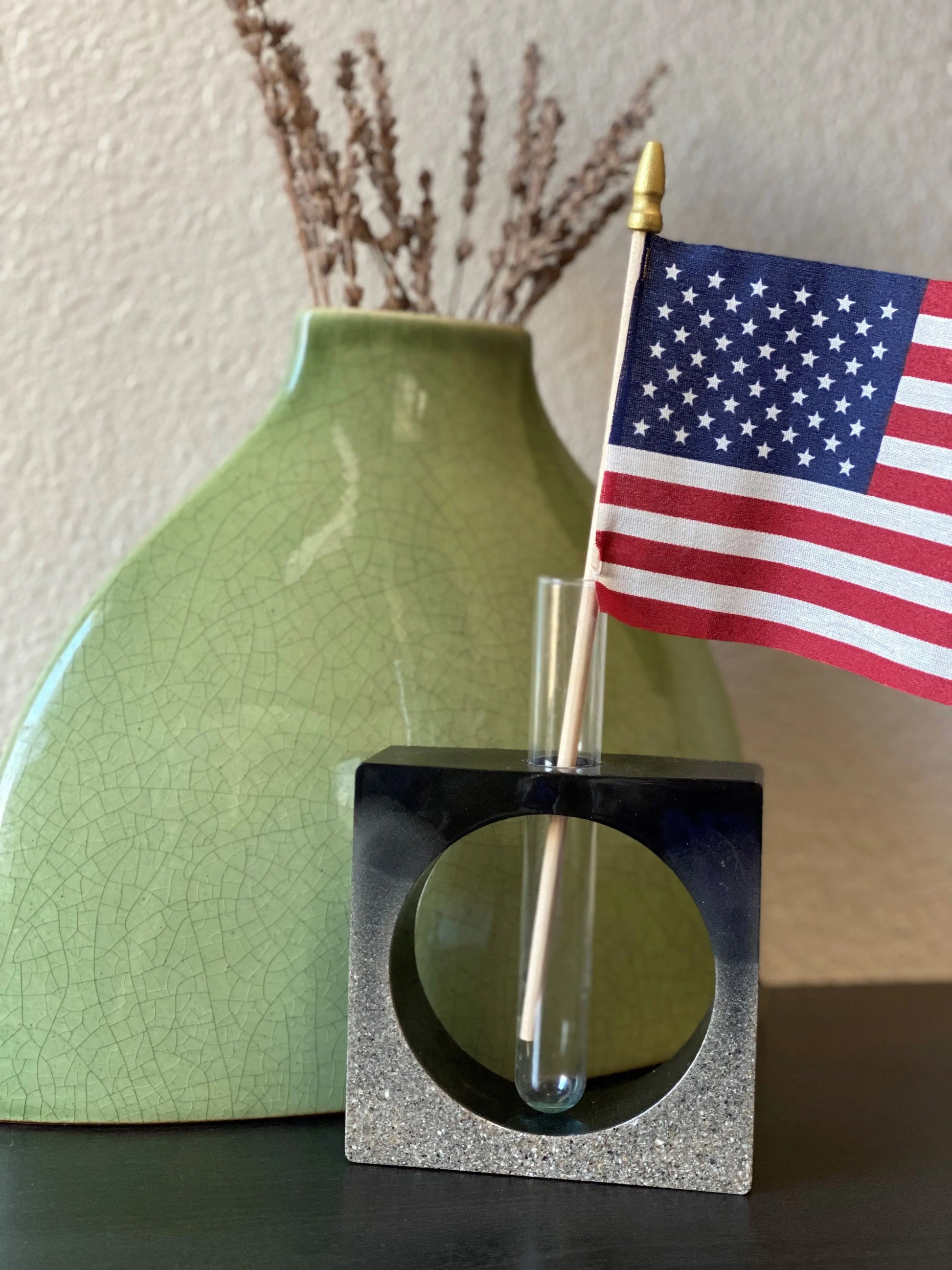 Small American flag in a decorative holder with a green vase in the background