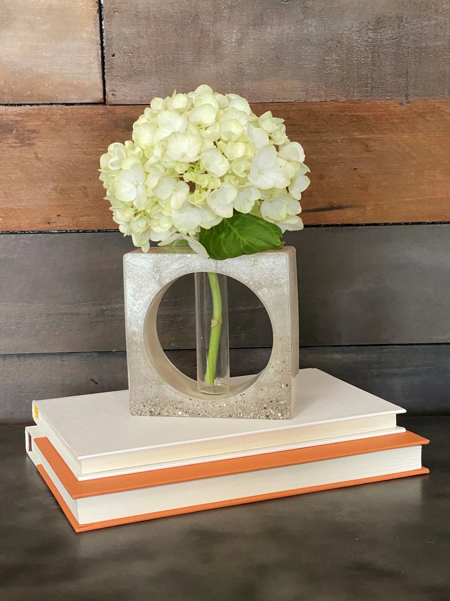 Ash infused vase with white flowers on a stack of books against a wooden background