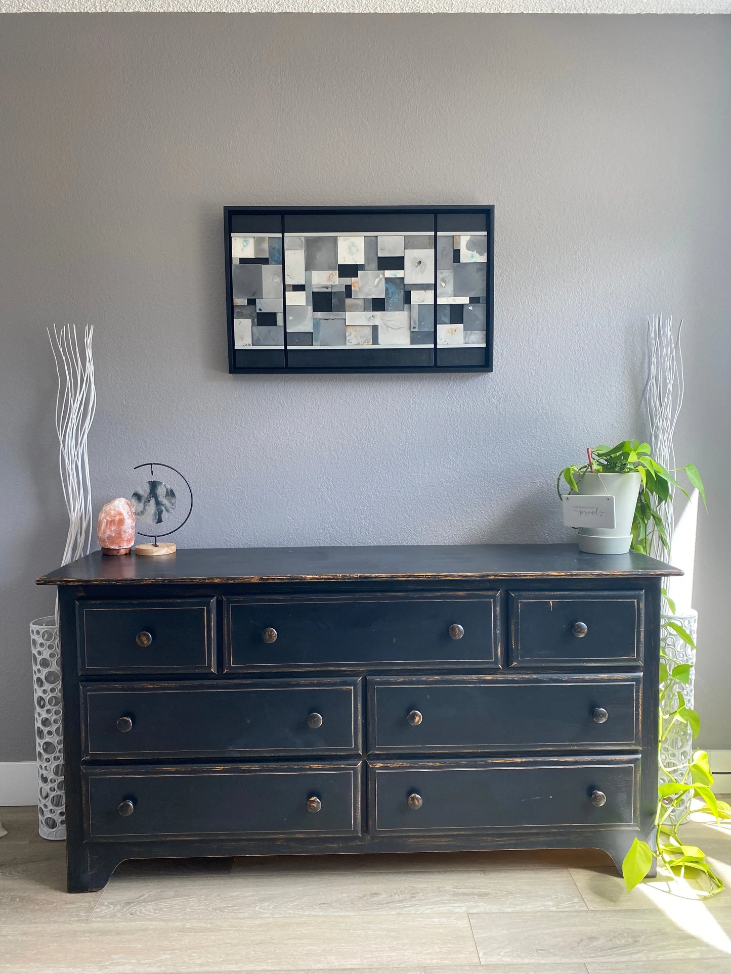 Dark dresser with multiple drawers against a gray wall, with a decorative wallart piect.