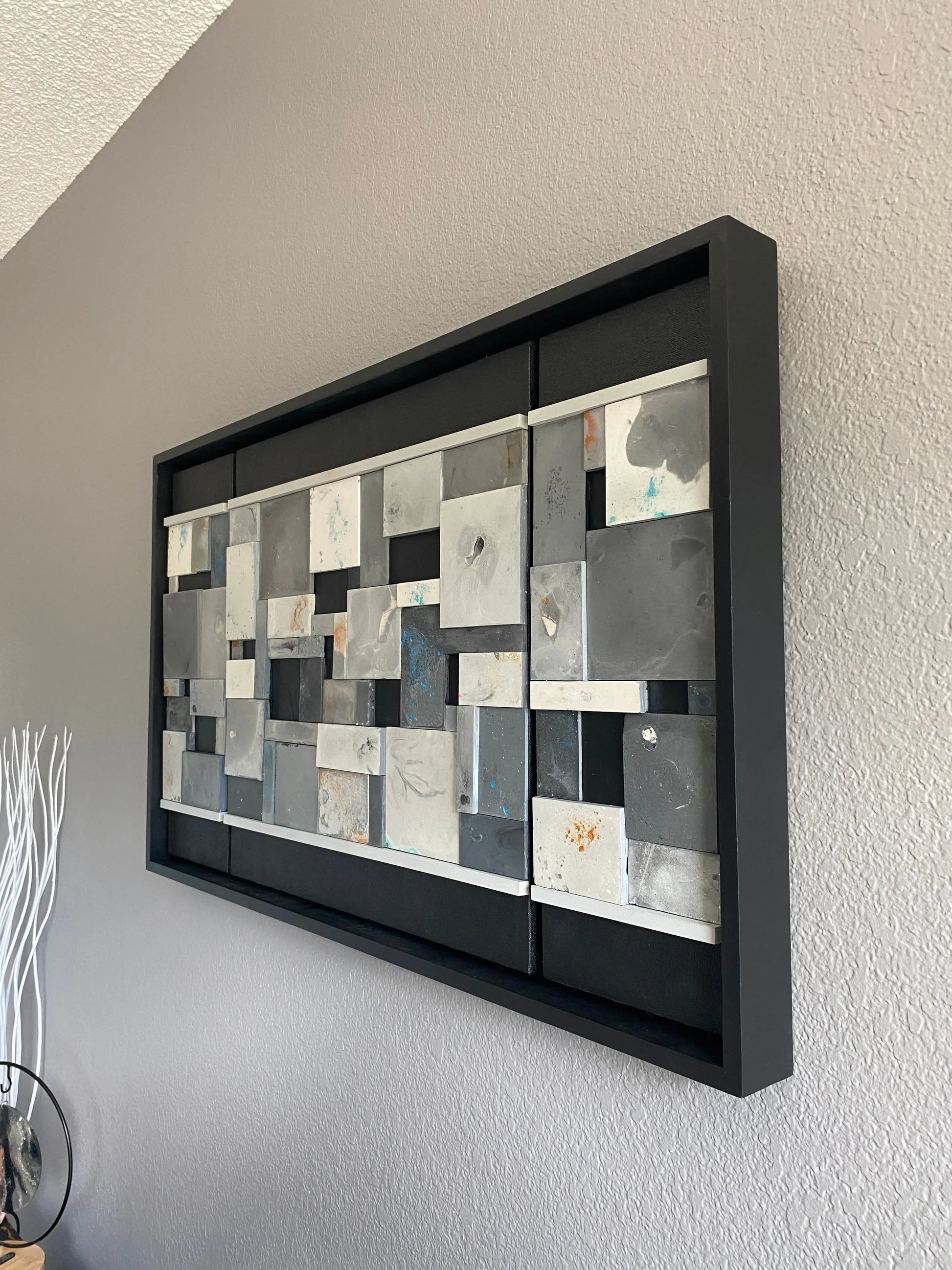 Decorative wallart with geometric pattern in a black frame on a plain wall.