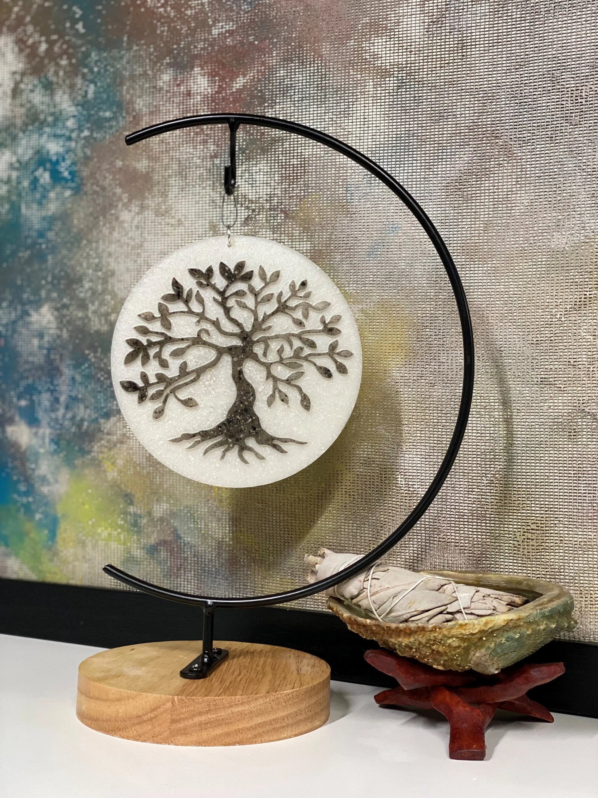 Decorative art with tree of life design on a stand against a textured wall.