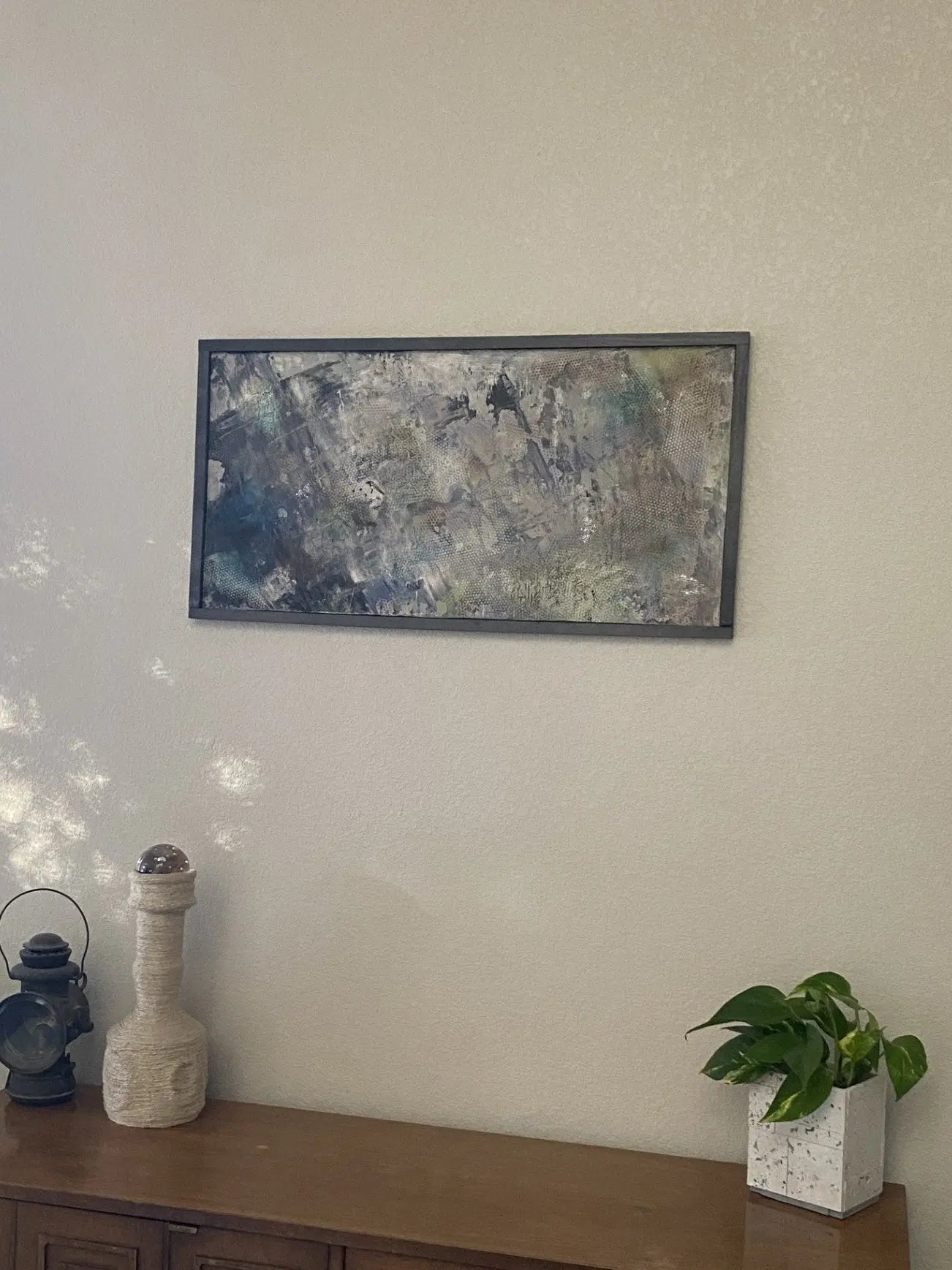 Abstract painting on a wall above a wooden cabinet with decorative items.